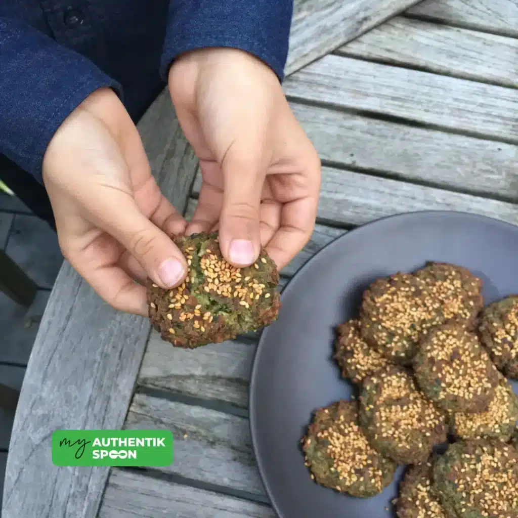 hands holding freshly baked falafel with plate in background