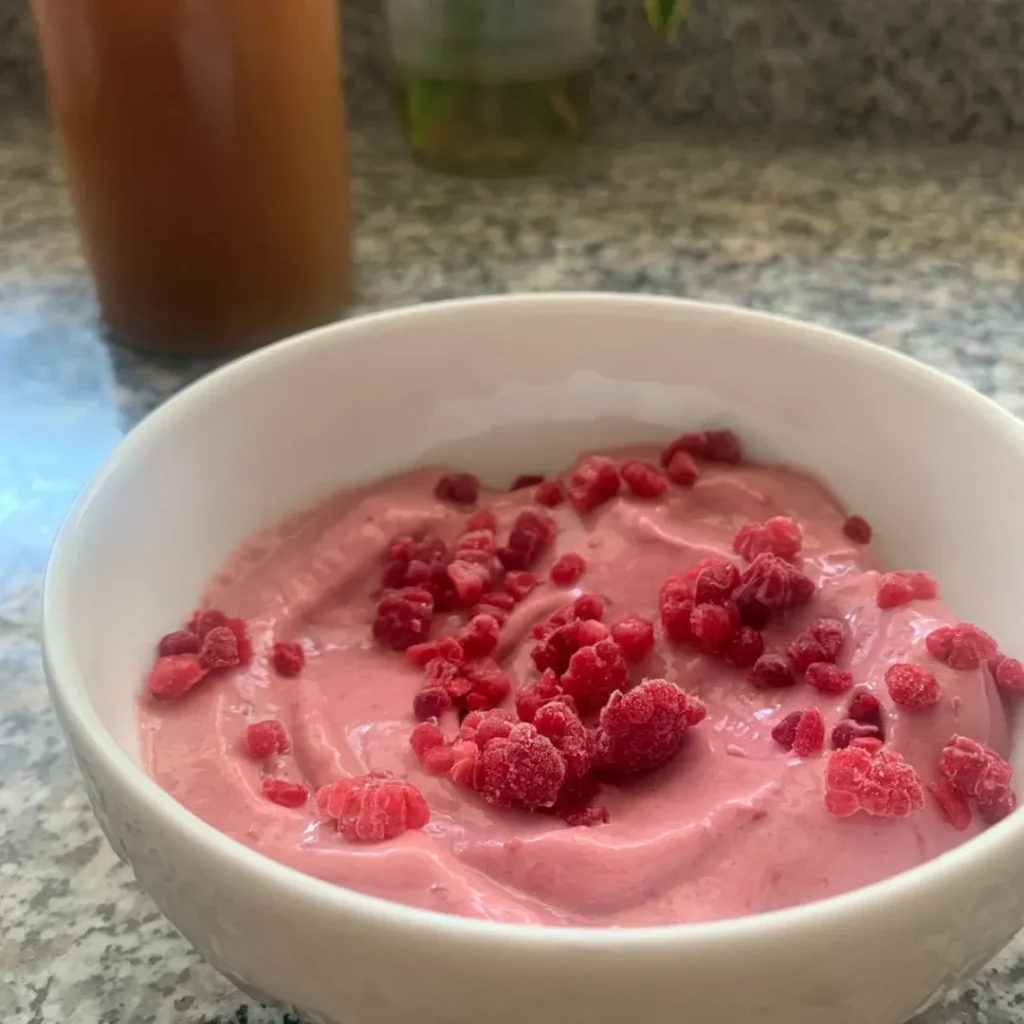 bone broth ice cream topped with frozen raspberries in a white bowl