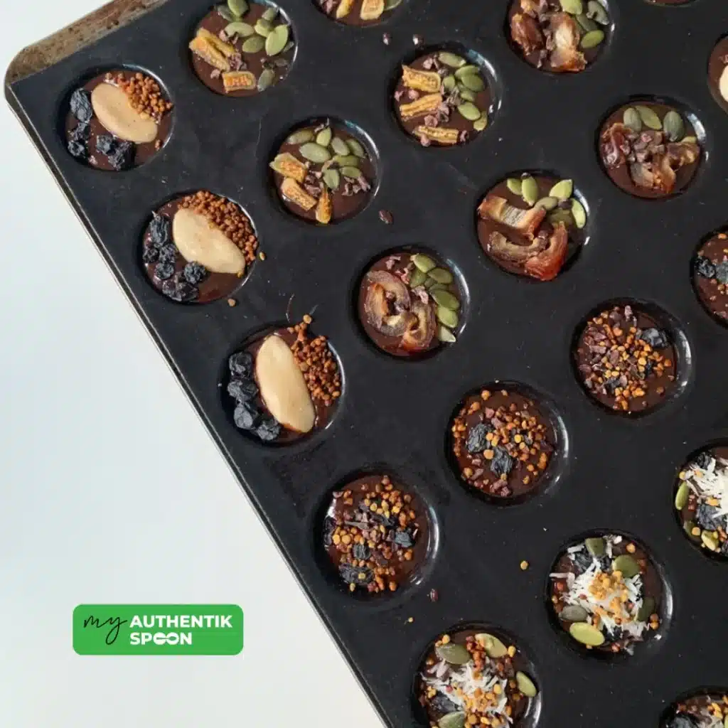 Homemade raw chocolate bites in a mold, topped with seeds, dried fruit, and superfoods