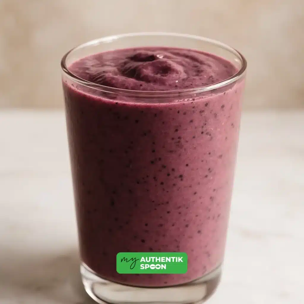 A vibrant purple glowing skin smoothie made with berries, flaxseeds, and avocado, served in a clear glass.
