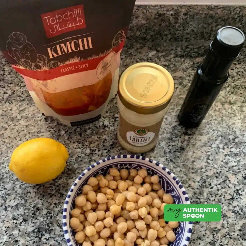Kimchi hummus ingredients with chickpeas, tahini, olive oil, garlic and fermented kimchi on kitchen table