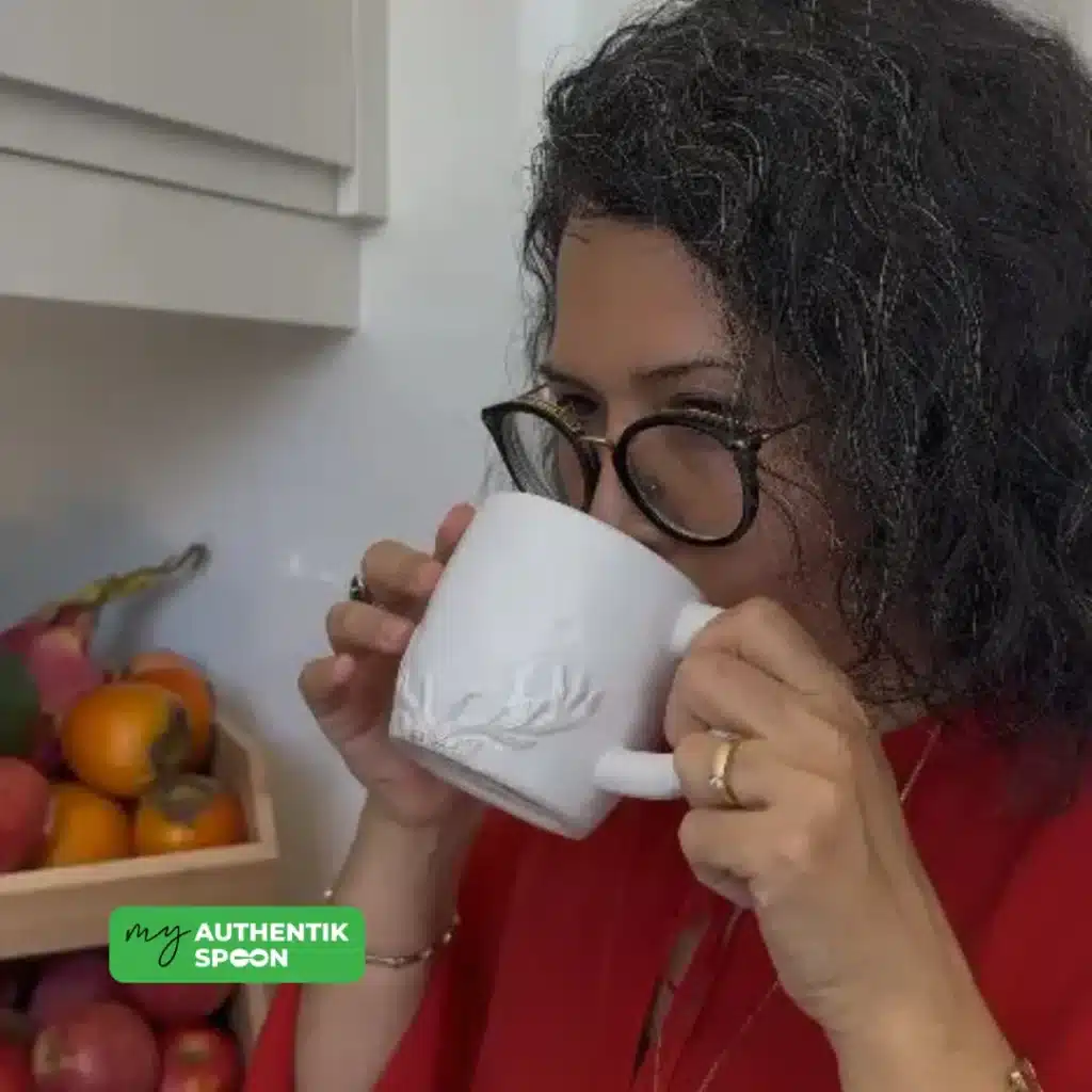 Woman sipping a warm lemon ginger morning drink to support digestion and energy.