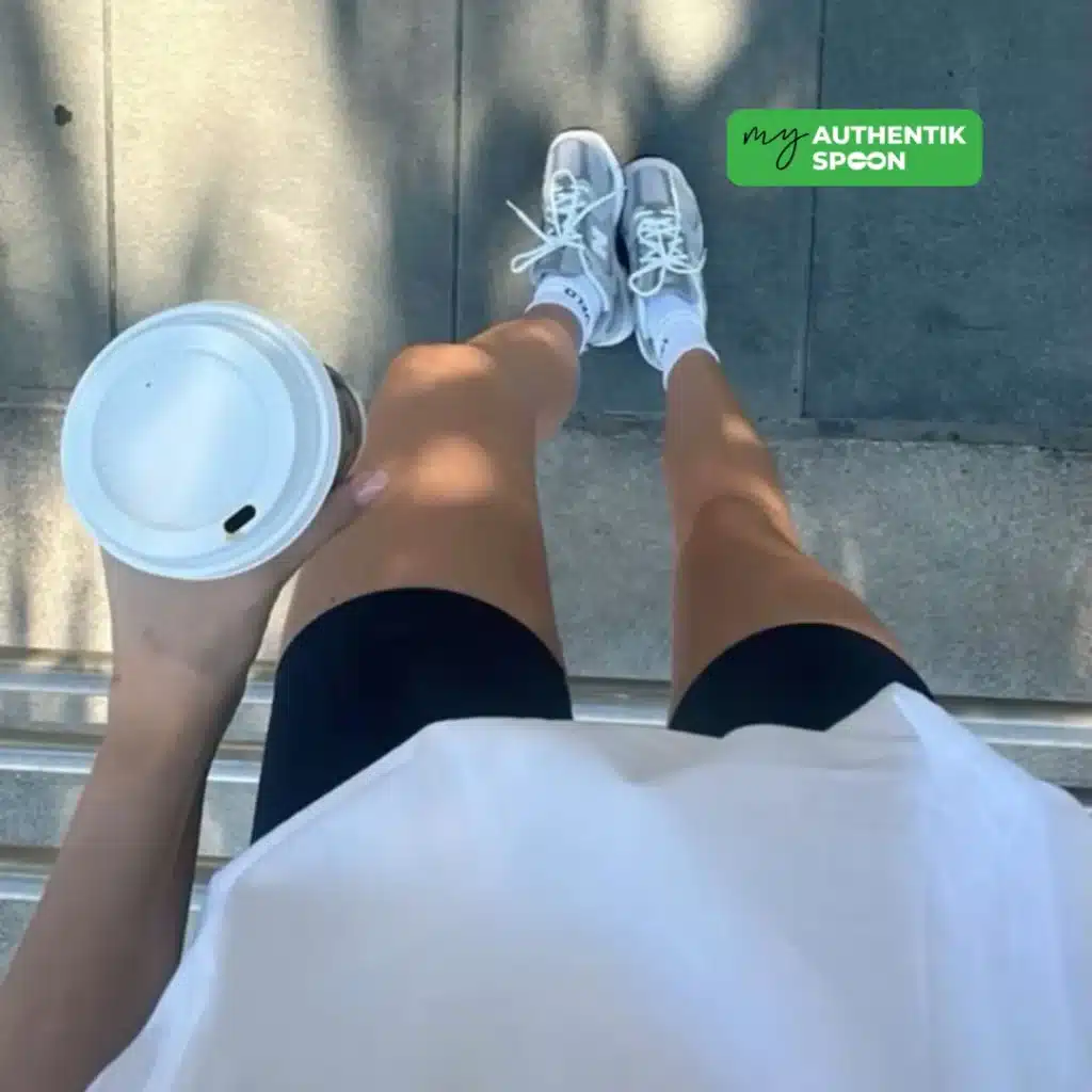 woman in workout clothes holding a coffee cup while standing on the street after a walk