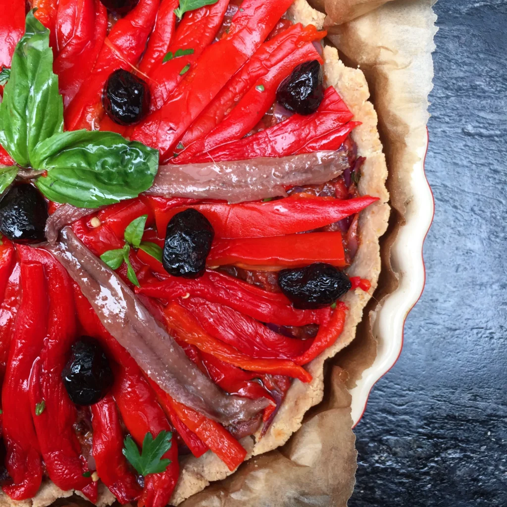 Roasted red pepper strips and black olives on a gluten free pissaladière