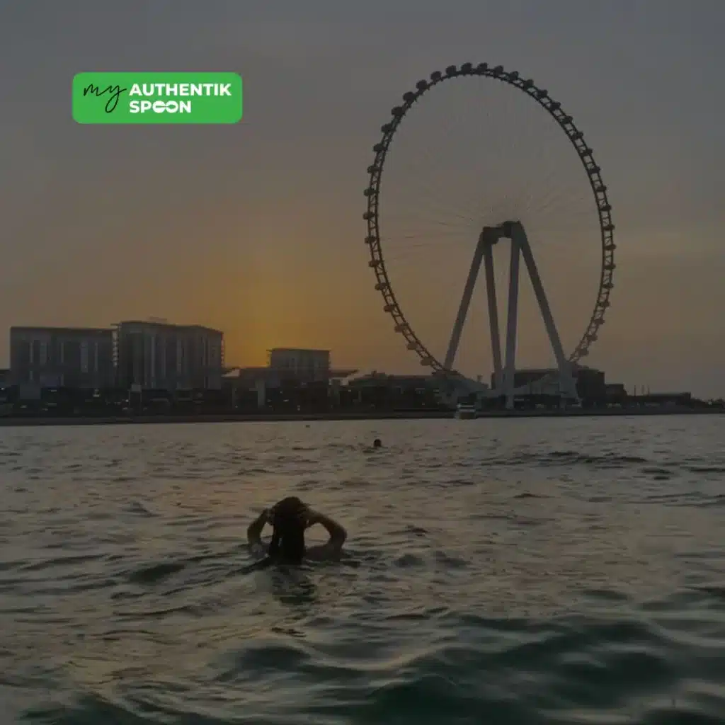 woman swimming in the sea at sunset in Dubai with Ain Dubai in the background