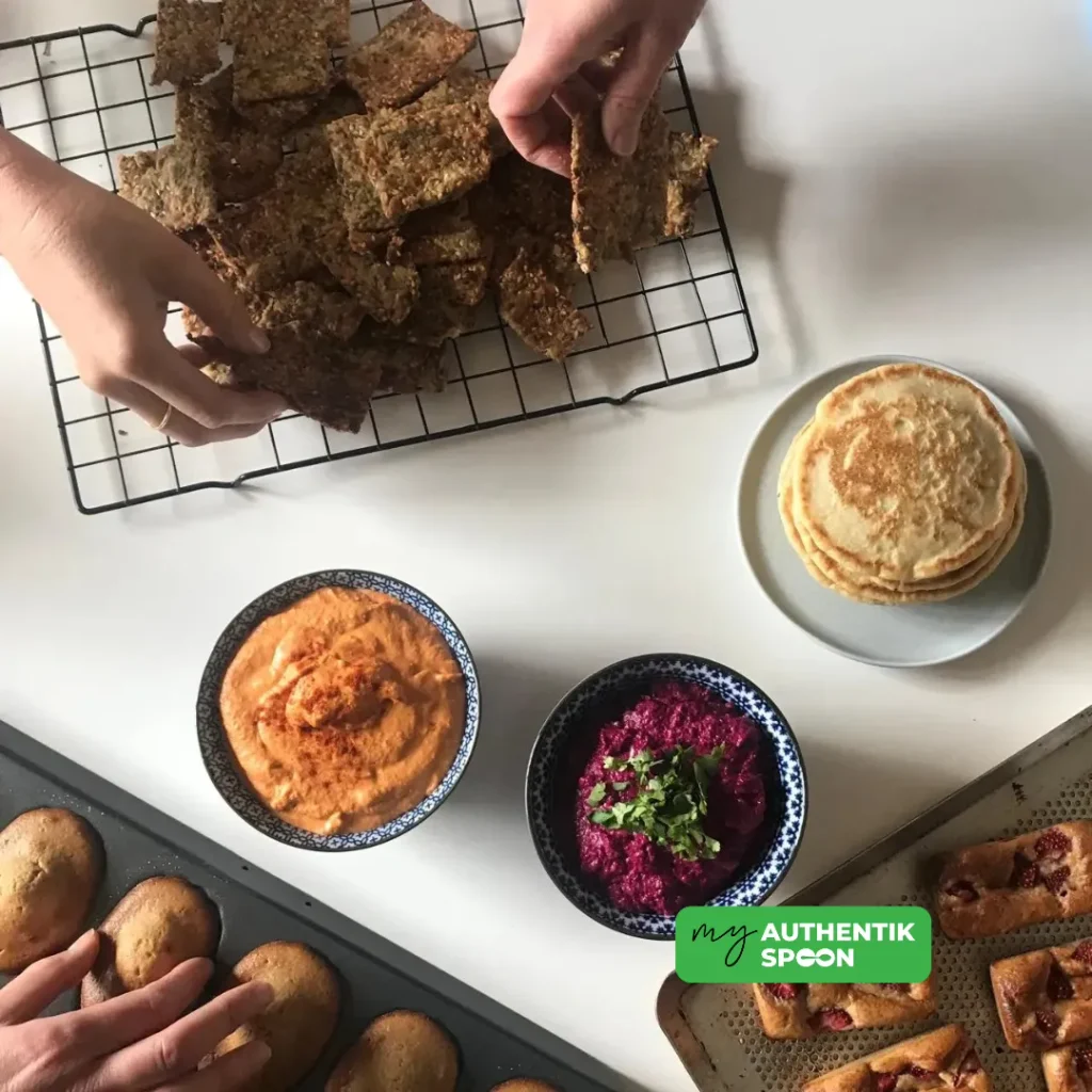 hands reaching for healthy seed crackers with roasted red pepper and beetroot dips