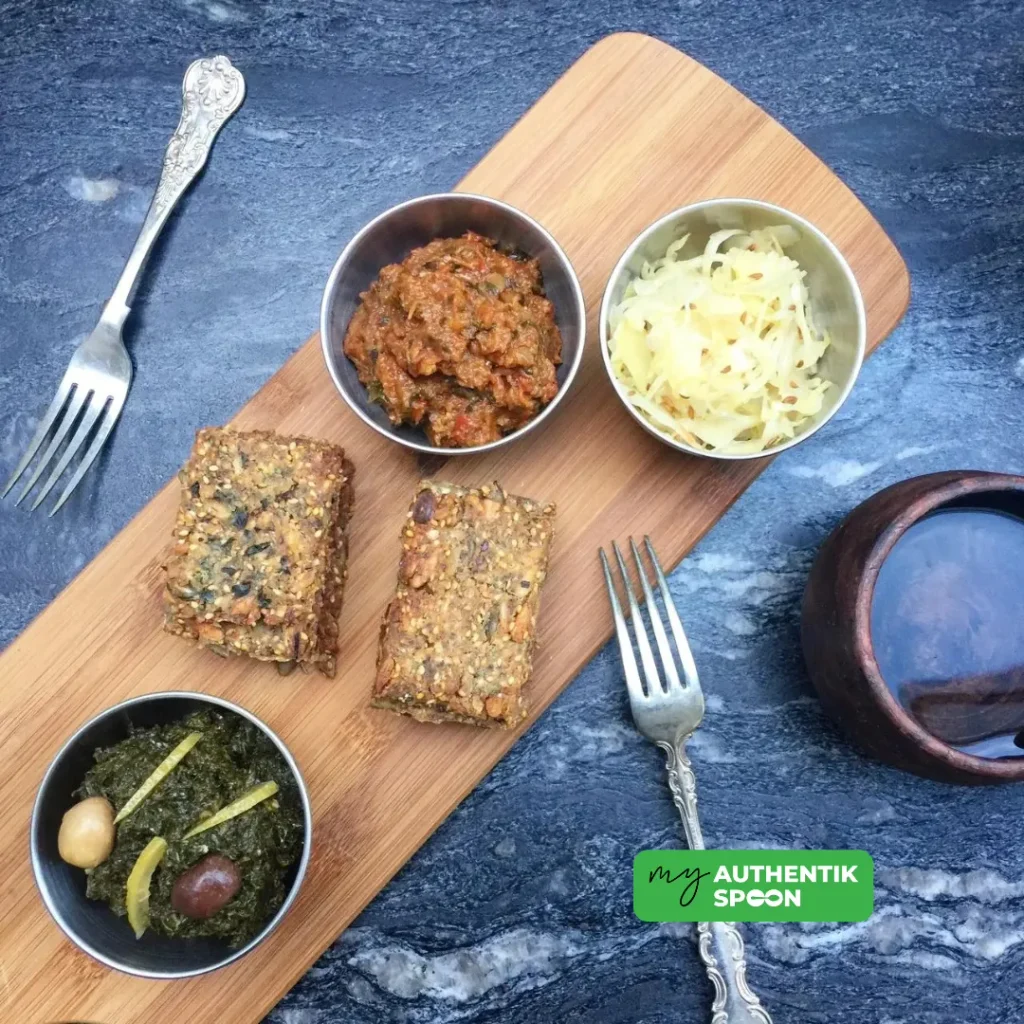 vegan seed crackers on a wooden board with sauerkraut, tomato aubergine salad and sautéed greens